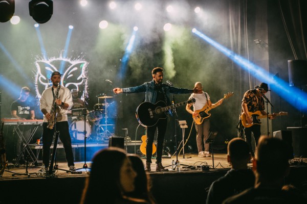 Banda completa en escenario con luces azules y logo Teína